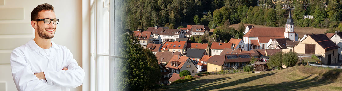 Junger Arzt schaut zufrieden aus dem Fentster auf ein Dorf.